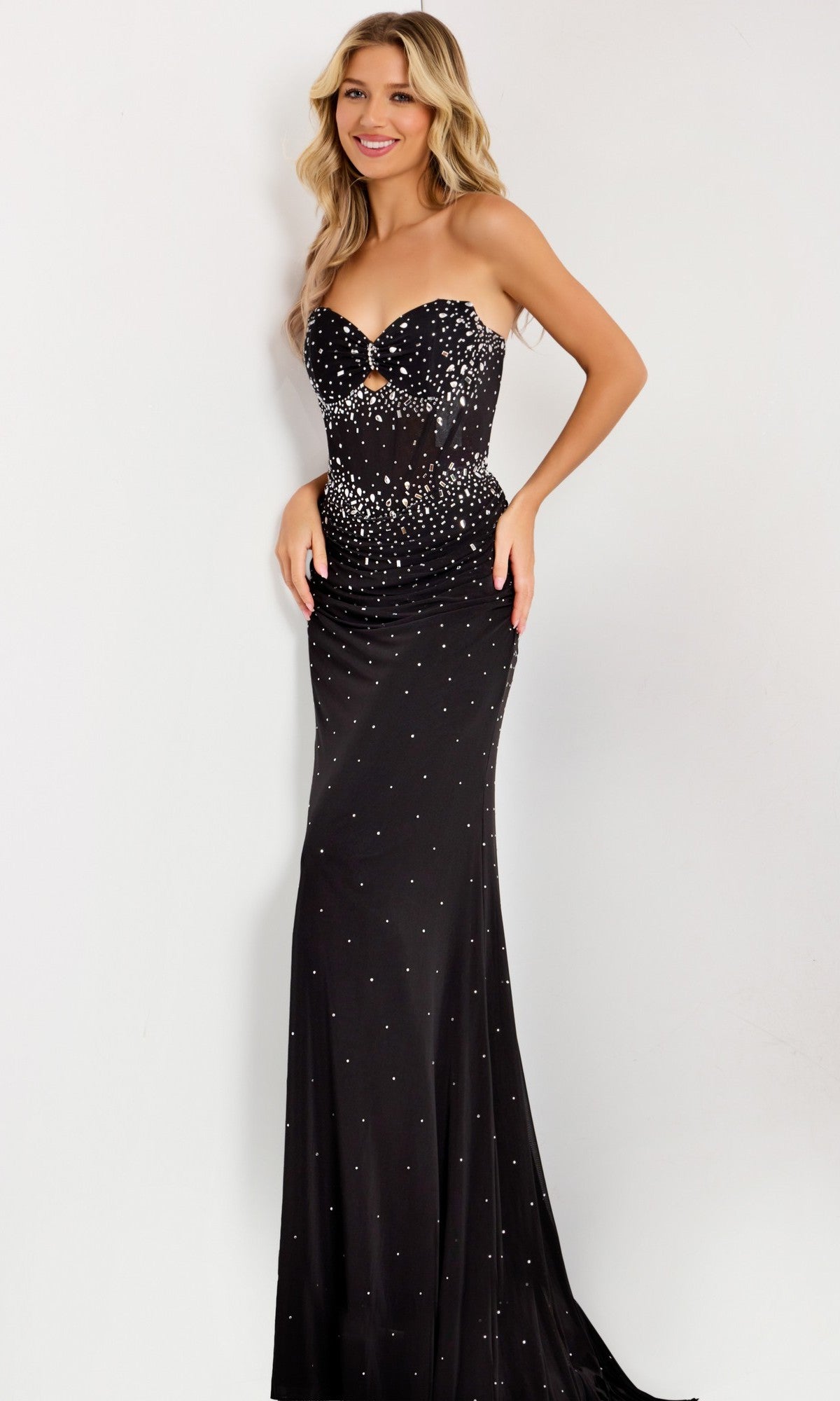 A woman in the Jovani 48372 long prom dress, featuring a strapless fitted bodice with sparkling rhinestone embellishments, stands against a plain light background, highlighting the gown's elegance.